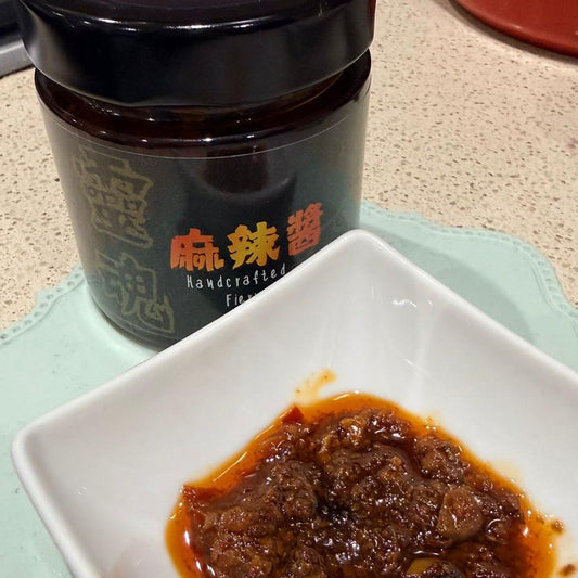 Jar of sauce with a spoon on a countertop next to a small dish of the same sauce.