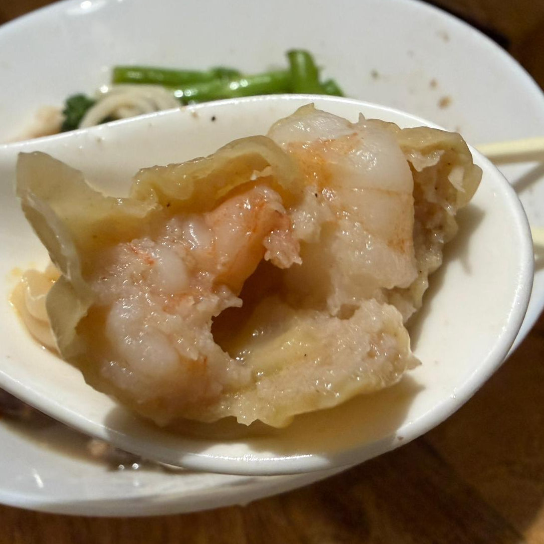 Spoon holding a dumpling with shrimp and meat, on a wooden table.