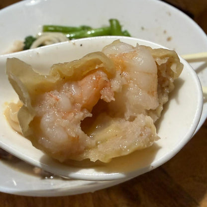 Spoon holding a dumpling with shrimp and meat, on a wooden table.
